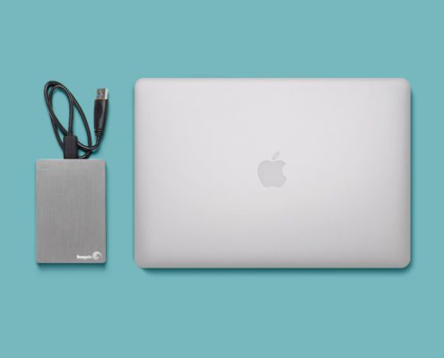 Laptop and external hard drive on turquoise background.
