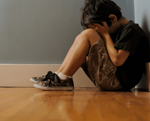 Child sitting alone, covering face in distress.