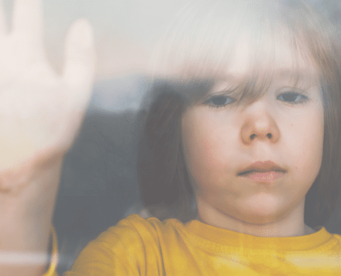 Child with hand on glass, looking outside.