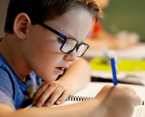 Boy writing in a notebook, wearing glasses.