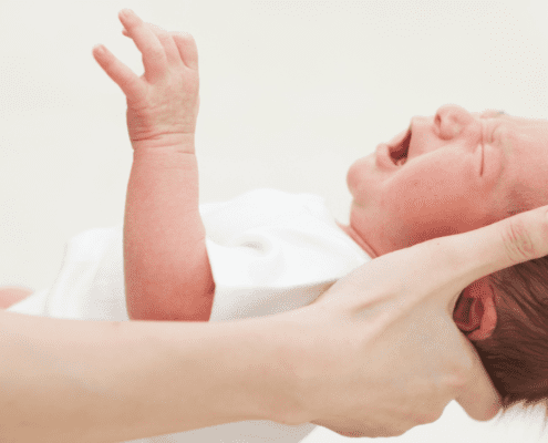 Crying newborn held by an adult's hand.