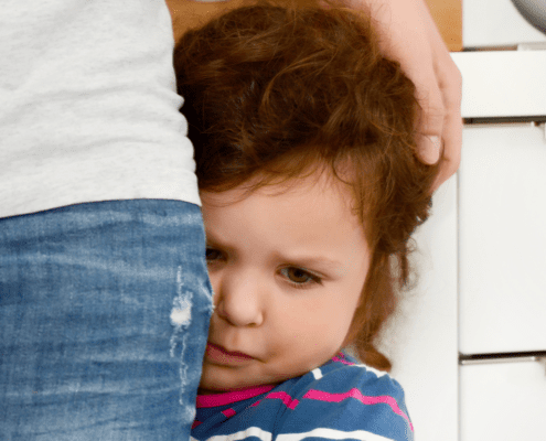 Child hugging adult's leg, looking scared.