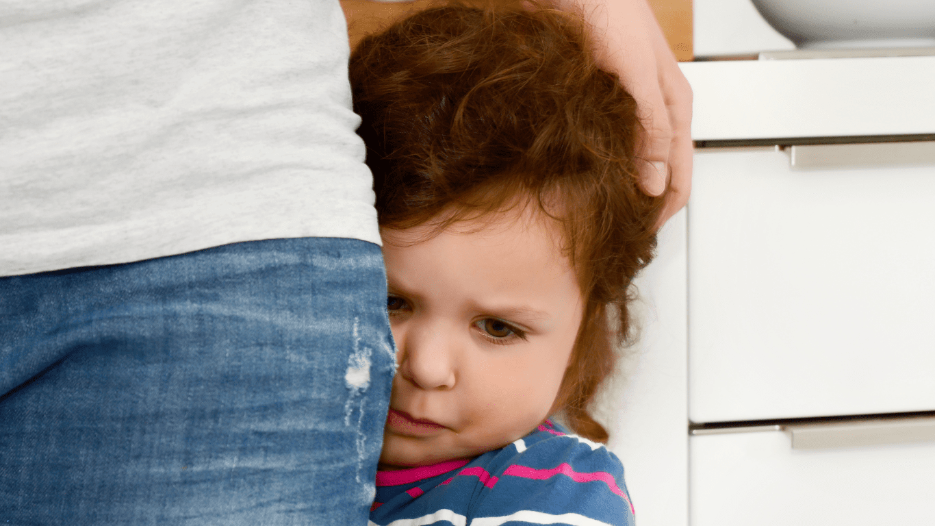 Child hugging adult's leg, looking scared.