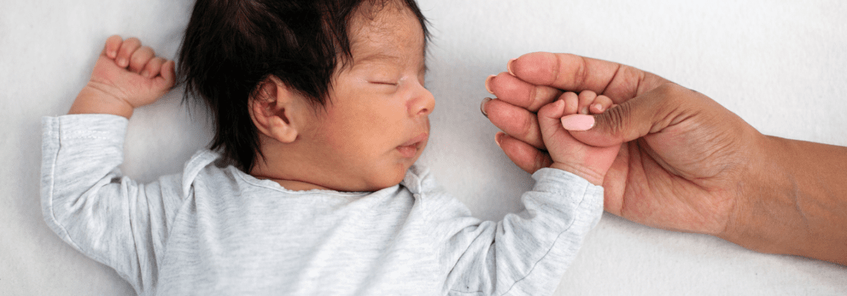 Sleeping newborn holding an adult's hand.