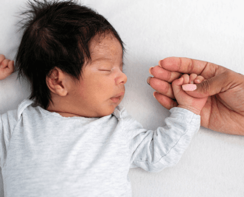 Sleeping newborn holding an adult's hand.