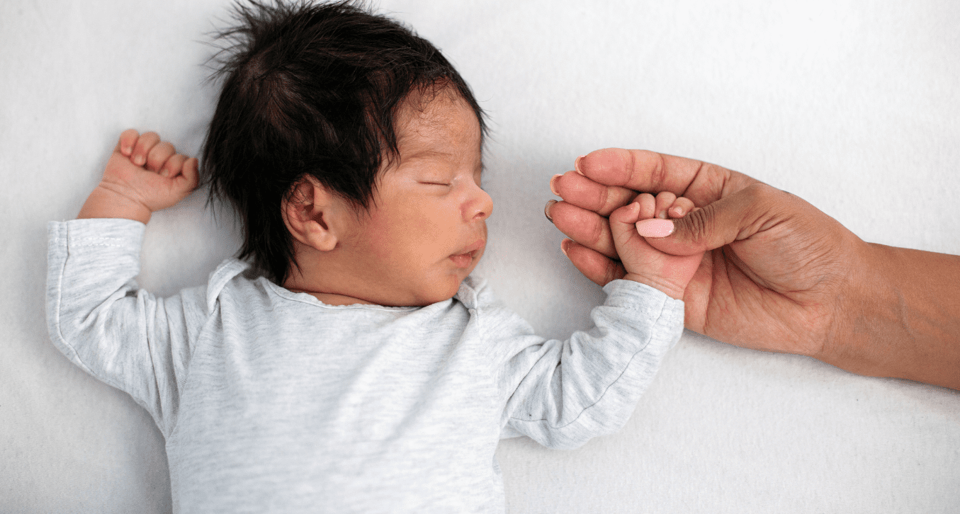 Sleeping newborn holding an adult's hand.