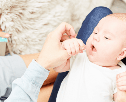 Baby holding hand, lying on parent's lap.