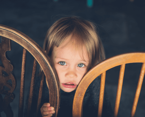 Child peeking between two wooden chairs.