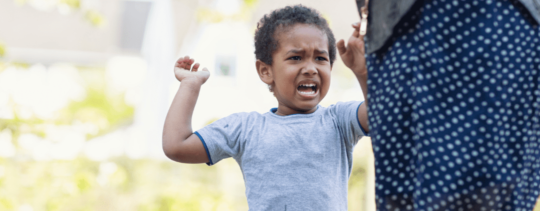 Child upset outdoors with adult nearby.