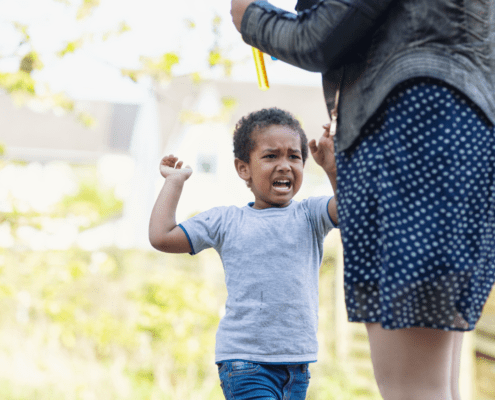 Child upset outdoors with adult nearby.