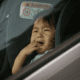 Crying child in car seat, looking outside.