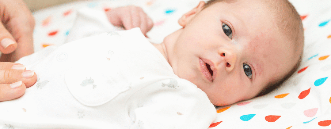 Baby lying on colorful blanket, awake.