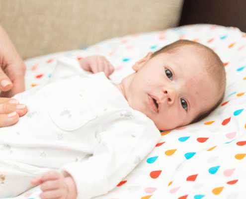 Baby lying on colorful blanket, awake.