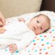 Baby lying on colorful blanket, awake.