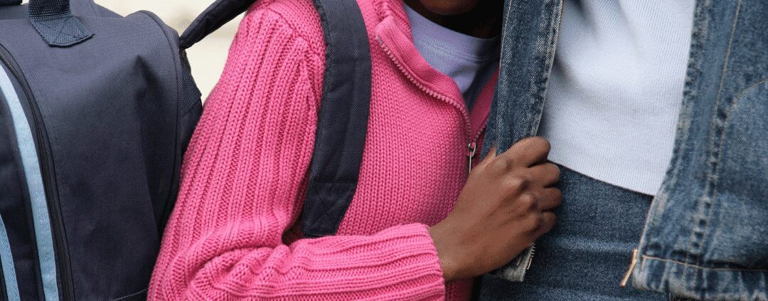 Child with backpack holding adult's hand.