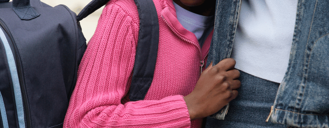 Child with backpack holding adult's hand.