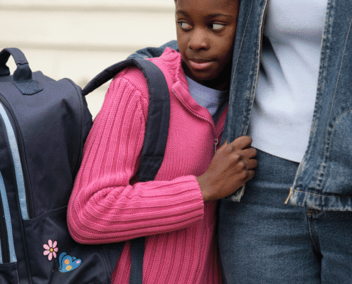 Child with backpack holding adult's hand.