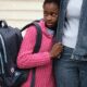 Child with backpack holding adult's hand.