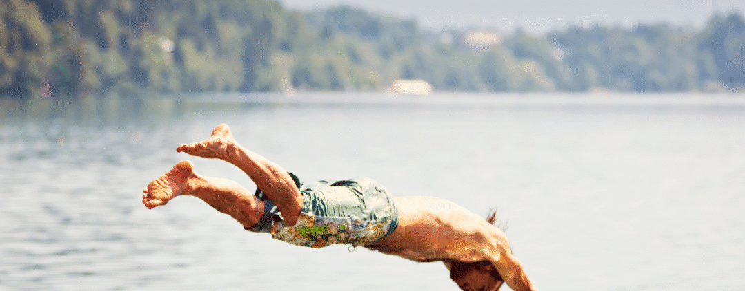 Person diving into a lake, mountains background.