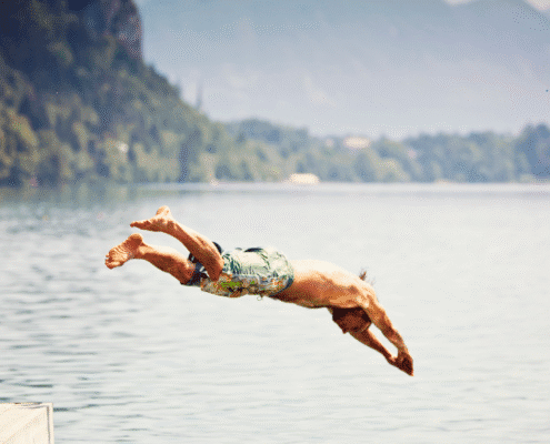Person diving into a lake, mountains background.
