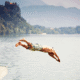 Person diving into a lake, mountains background.