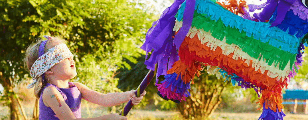 Child hitting colorful piñata outdoors.