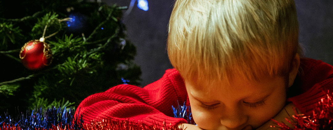 Child asleep near Christmas tree decorations.
