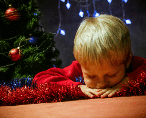 Child asleep near Christmas tree decorations.