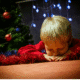 Child asleep near Christmas tree decorations.