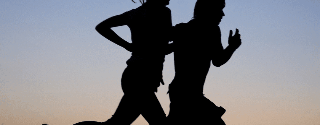 Silhouettes of two people running at sunset.