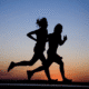 Silhouettes of two people running at sunset.