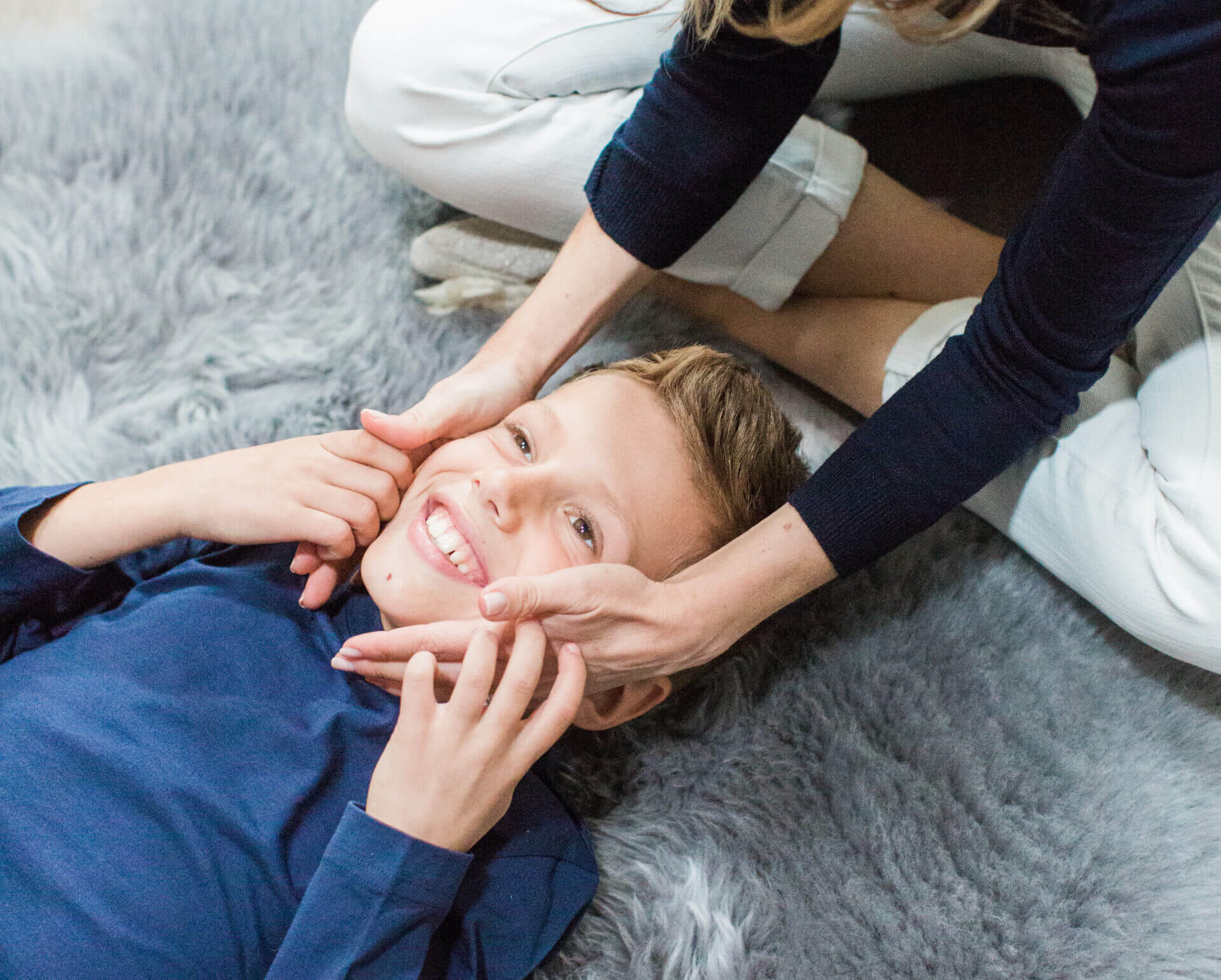 Child smiling while lying on grey rug.