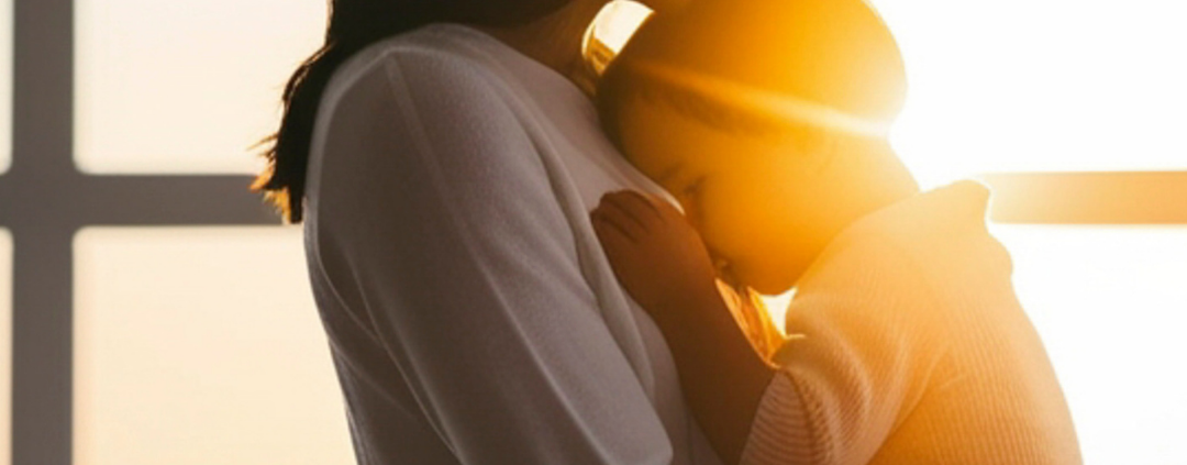 Mother and child embracing by window sunset.