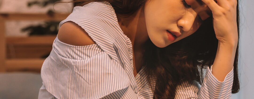 Woman sitting on bed holding her head
