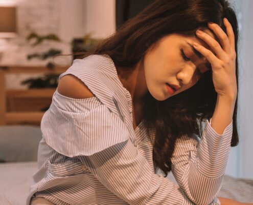Woman sitting on bed holding her head
