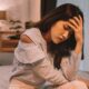 Woman sitting on bed holding her head